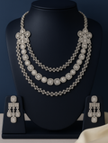 Silver necklace and earrings set on a black stand with a dark blue background