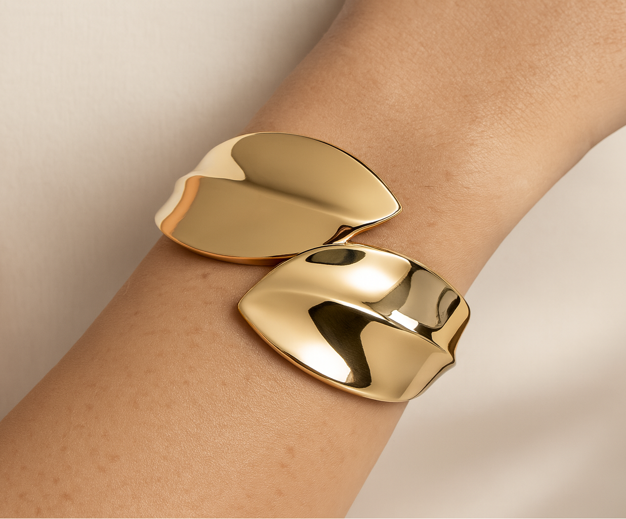 Gold cuff bracelet on a wrist against a neutral background