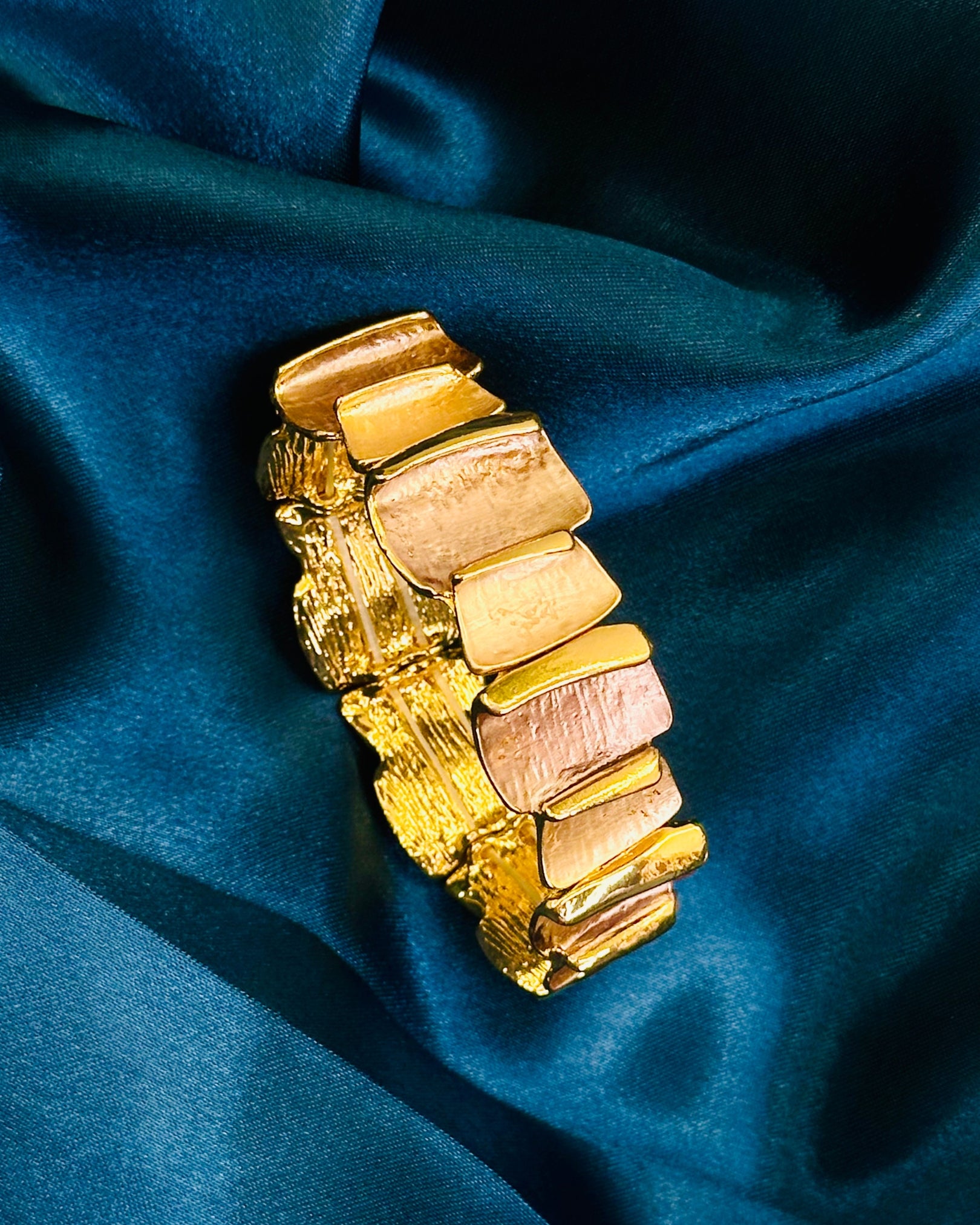 Gold bracelet with a textured design on a blue fabric background